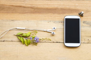 ahşap arka plan üzerinde mor çiçekli beyaz cep telefonu kulaklık