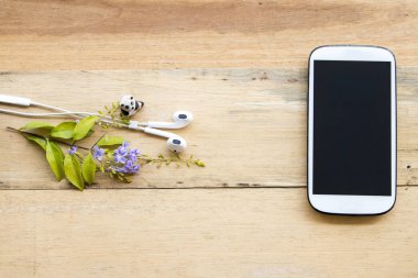 ahşap arka plan üzerinde mor çiçekli beyaz cep telefonu kulaklık