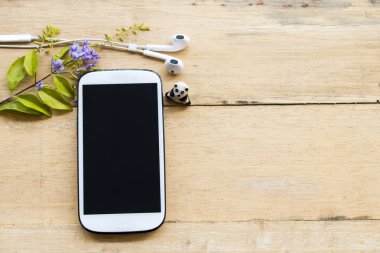 ahşap arka plan üzerinde mor çiçekli beyaz cep telefonu kulaklık