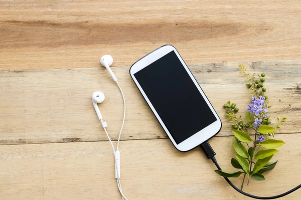 ahşap arka plan üzerinde mor çiçekli beyaz cep telefonu kulaklık ve şarj edilebilir piller kordon
