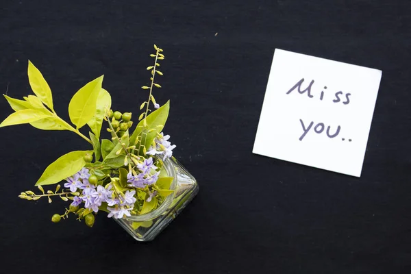 i miss you message card with purple flowers in bottle on background black