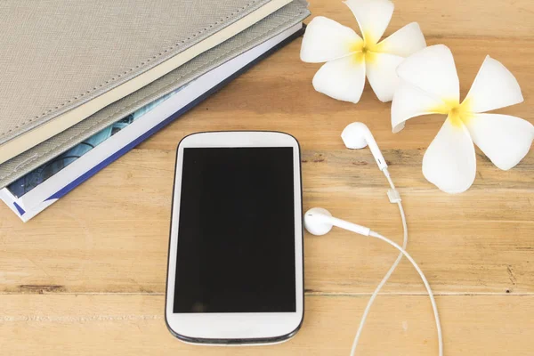 notebook planner  with mobile earphone for business and white flower frangipani on background white at office desk