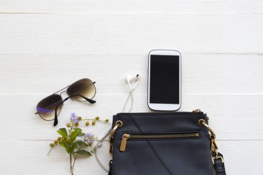 mobile phone ,sunglasses and shoulder bag collection of lifestyle woman relax arrangement flat lay style on background white wooden