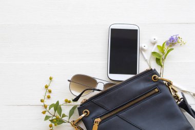 mobile phone ,sunglasses and shoulder bag collection of lifestyle woman relax arrangement flat lay style on background white wooden
