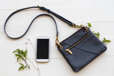 Cep telefonu, omuz çantası yaşam tarzı kadın aksesuarları rahatlama düzenleme düz arka plan beyaz ahşap üzerine yatar