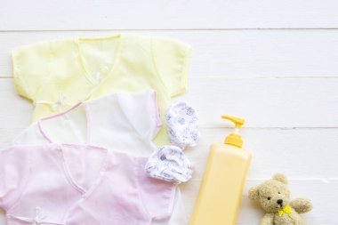 Yeni doğmuş bebek ve kız çocuğunun pamuklu giysileri vücut bakımı için vücut losyonu ile temizlenmiş cilt bakımı için düz arka planda beyaz ahşap üzerinde yatıyordu.