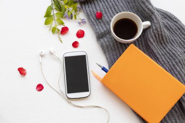 defter, cep telefonu, kahve ve örgü yün ören hayat kadını kış mevsimi dekorasyonunda arka planda beyaz ahşap üzerine rahatla.