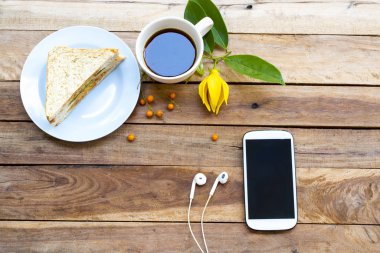 Kahvaltılı cep telefonu sıcak kahve espresso, sanviç ve sarı çiçek ylang ylang düzenleme düz zemin üzerinde yatıyordu ahşap