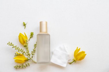 İlk terapi, pamuk doğal kozmetik içeren serum tonerleri cilt için bitkisel sağlık hizmetleri sunar. Kadın yüzü güzelliği ve sarı çiçek ylang ylang düzenleme düz zemin üzerinde yatar. 
