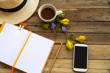 Not defteri günlüğü, cep telefonu ve iş için sıcak kahve sarı çiçek ylang ylang, hayat tarzı kadın şapkası rahatlama düzenleme düz arka plan ahşap üzerinde yatıyordu