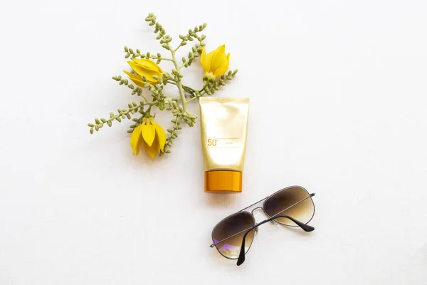 Güneş kremi spf50 yaşam tarzı kadın güneş gözlüklü cilt bakımı ve çiçek ylang düzenleme düz arka plan beyaz üzerine yatıyordu 