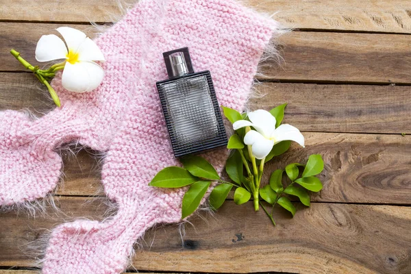 black bottle perfume with pink knitting wool scarf ,flowers frangipani of lifestyle woman relax arrangement flat lay style on  background wooden