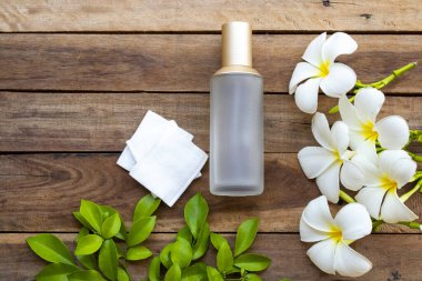 Terapi, pamuk doğal kozmetik içeren ilk serum tonerleri, cilt için bitkisel sağlık hizmetleri sunar. Kadın ve çiçek frangipani düzenlemesinin güzelliği, arka plandaki ahşap düzlükte yatar.