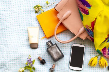 Parfüm, sarı eşarp, güneş gözlüğü, oje, güneş kremi, defter, cep telefonu ve pembe el çantası aksesuarları.