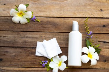 Terapi, pamuk doğal kozmetik içeren ilk serum tonerleri, cilt için bitkisel sağlık hizmetleri sunar. Kadın ve çiçek frangipani düzenlemesinin güzelliği, arka plandaki ahşap düzlükte yatar.