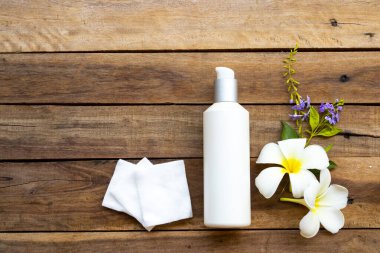 Terapi, pamuk doğal kozmetik içeren ilk serum tonerleri, cilt için bitkisel sağlık hizmetleri sunar. Kadın ve çiçek frangipani düzenlemesinin güzelliği, arka plandaki ahşap düzlükte yatar.