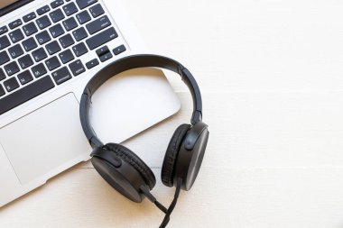 Siyah kulaklıklı bilgisayar defteri arka plandaki yaşam tarzını dinliyor beyaz ahşap