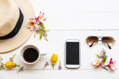 cep telefonu, sade kahve espresso, güneş gözlükleri, şapka ve çiçek ylang ylang, frangipani, bahar sezonu aranjmanında mor çiçekler arka plan beyaz ahşap üzerine serili.