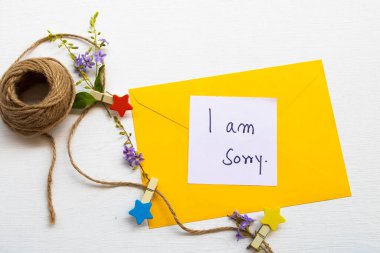 Yalnız değilsiniz. Sarı zarf, ahşap yıldız, ip ve mor çiçek aranjmanı içeren el yazısı. Arka planda beyaz ahşap bir kartpostal şeklinde.