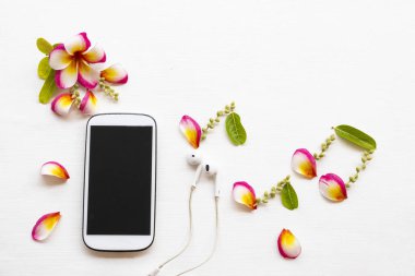 cep telefonu, kulaklık çiçek yapraklı frangipani aranjman müziği düz fon beyaz ahşap üzerine yatıyordu
