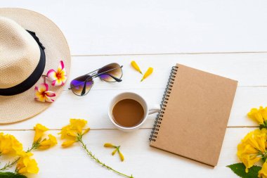 Sıcak kahveyle, sarı çiçeklerle, şapkayla, hayat tarzı kadınının güneş gözlükleriyle iş planlayıcısı yaz sezonu düzenlemelerinde rahatla düz bir şekilde arka planda beyaz ahşap üzerine uzan.
