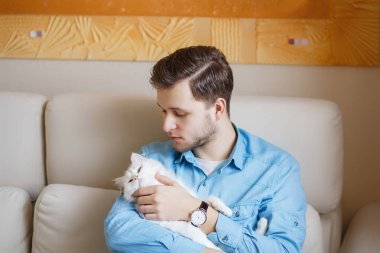 Mavi gömlekli beyaz kabarık kedi ile oynarken, çekici bir adam