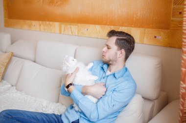 Mavi gömlekli beyaz kabarık kedi ile oynarken, çekici bir adam