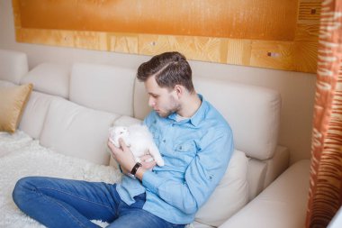 Mavi gömlekli beyaz kabarık kedi ile oynarken, çekici bir adam