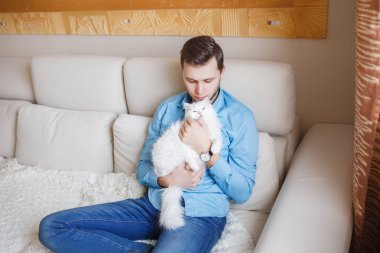 Mavi gömlekli beyaz kabarık kedi ile oynarken, çekici bir adam