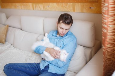 Mavi gömlekli beyaz kabarık kedi ile oynarken, çekici bir adam