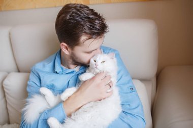 Mavi gömlekli beyaz kabarık kedi ile oynarken, çekici bir adam