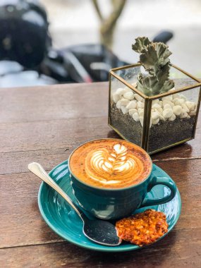 Bir fincan kahve bir kafede bir kaktüs ile ahşap bir masa üzerinde duruyor.
