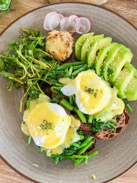 A useful green breakfast on a wooden table. Eggs poached, or eggs in Florentine. Rucola, avocado, whole wheat bread. Dishes under the color of the tree.