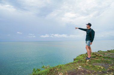Sırt çantası, bir uçurumun üzerinde duran ve elini uzaklık işaret olan genç bir adam. O bir hedef belirler.