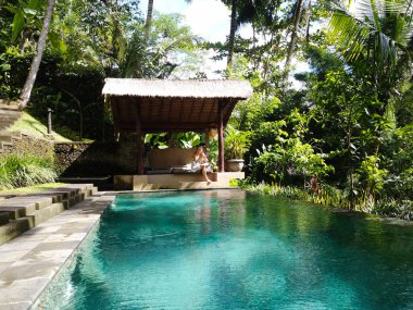 Genç bir kız bir çardak masmavi su ile sonsuzluk havuz kenarında oturuyor. Villa Ada Bali Ubud ormanda.
