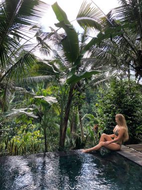 Genç bir kız ormanda bir sonsuzluk havuzu kenarında oturur. Ubud Bali Adası üzerinde gerçekleştirilen.