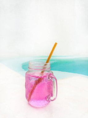 Pembe içmek - pembe bir şeffaf cam ahşap pipet havuzun arka plan ve beyaz bir arka plan ile. Kopya alanı ile yan görünüm