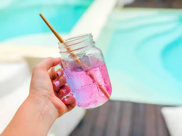 Pink drink - karkade in a transparent glass with a wooden straw on the background of the pool and on a white background. Side view with copy space