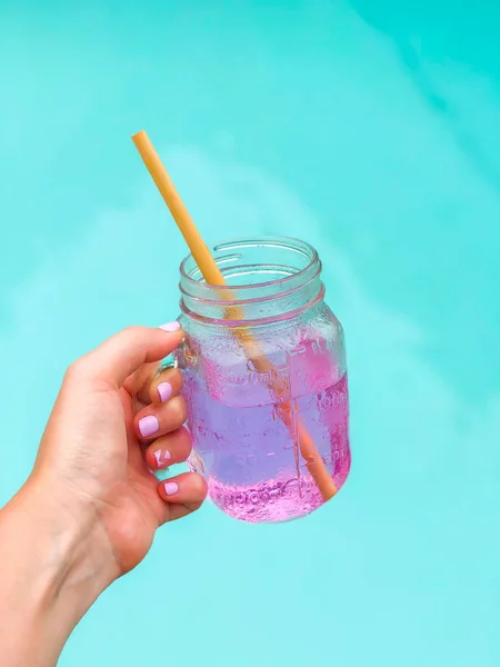 粉红色的饮料 Karkade 在一个透明的玻璃 在游泳池的背景和白色背景的木质稻草 带有复制空间的侧面视图 — 图库照片
