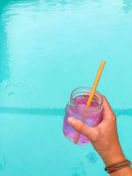 Pink drink - karkade in a transparent glass with a wooden straw on the background of the pool and on a white background. Side view with copy space