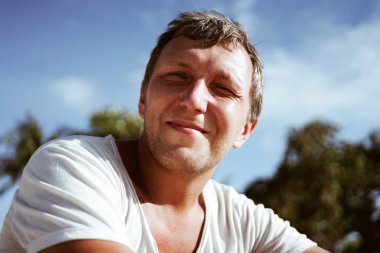 Sahilde oturup mutlu bir orta yaşlı adam portresi. Kafasında biraz gri saç.