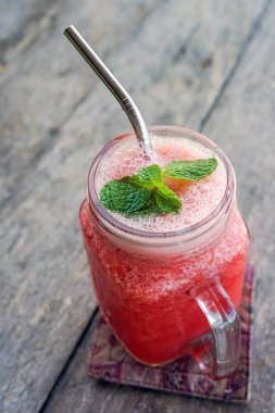 Kırmızı ahşap bir masa ve bir demir tübül içmek için kare bir fincan nane yaprağı suyuyla. Kopya alanı ile yan görünüm