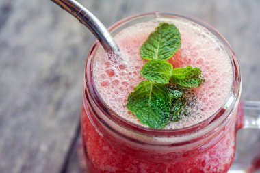 Kırmızı ahşap bir masa ve bir demir tübül içmek için kare bir fincan nane yaprağı suyuyla. Kopya alanı ile yan görünüm