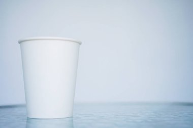 Bir beyaz kağıt (bir kerelik) bardak kahve için geçerli. Arka plan bulanık, beyaz ve mavi. Camına başlığı için yerleştirin. Kopya alanı ile yan görünüm