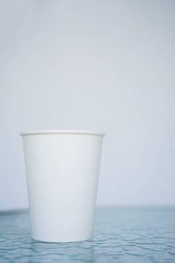 Bir beyaz kağıt (bir kerelik) bardak kahve için geçerli. Arka plan bulanık, beyaz ve mavi. Camına başlığı için yerleştirin. Kopya alanı ile yan görünüm