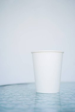 Bir beyaz kağıt (bir kerelik) bardak kahve için geçerli. Arka plan bulanık, beyaz ve mavi. Camına başlığı için yerleştirin. Kopya alanı ile yan görünüm