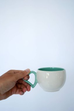 Beyaz bir adamın elini bir beyaz-yeşil kupa kahve veya çay için beyaz ve mavi bir duvara tutar. Kopya alanı ile yan görünüm