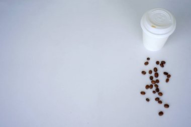 Tek kullanımlık bir fincan kahve kahve çekirdekleri ile beyaz çini üzerinde duruyor. Kopya alanı ile Üstten Görünüm