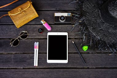 Koyu ahşap arka plan dijital tablet ile izole Minimal tarz düz yatıyordu. Kadın Danışma üstten görünüm aksesuarları ile: şapka, çanta, güneş gözlüğü, vintage fotoğraf makinesi, kulaklık, defter, kozmetik