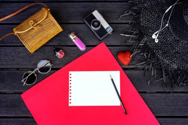 Minimal tarz düz izole üzerinde orijinal kırmızı ve koyu ahşap arka plan yattı. Kadın Danışma üstten görünüm aksesuarları ile: şapka, çanta, güneş gözlüğü, fotoğraf makinesi, kulaklık, defter, kozmetik. Kartpostal